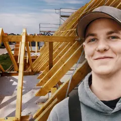 Junger Mann im Kapuzenpullover vor Dachstuhl. Informiert sich über zimmerer ausbildung gehalt netto.