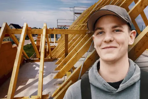 Junger Mann mit Kappe lächelt vor Dachstuhl. Ausbildung Zimmermann Gehalt ist ein guter Start.