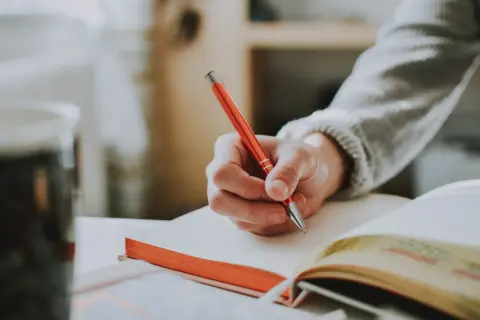Hand schreibt in ein Notizbuch. Die Person überlegt vielleicht, wie sie ihren **Dolmetscher Gehalt** optimieren kann.