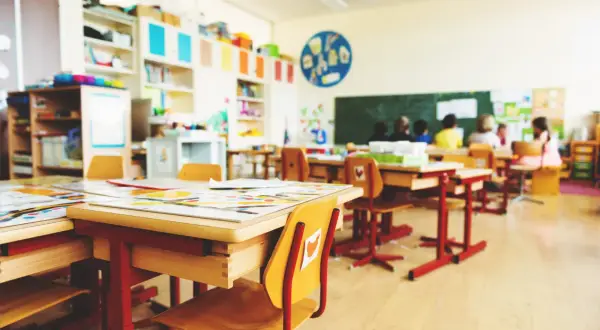Einladende Raumgestaltung im Klassenzimmer: Helle Tische, bunte Bücherregale und Kinder, die lernen.