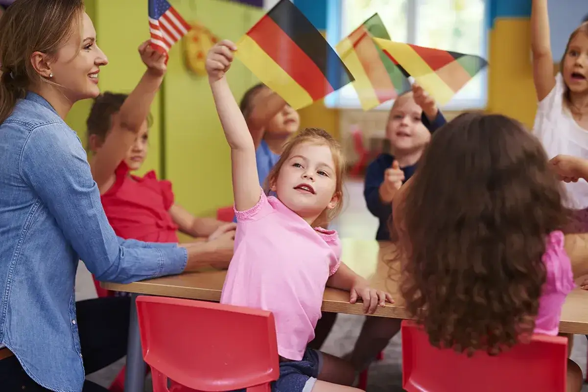 Lehrerin und Kinder mit deutschen und US-Flaggen im Unterricht.