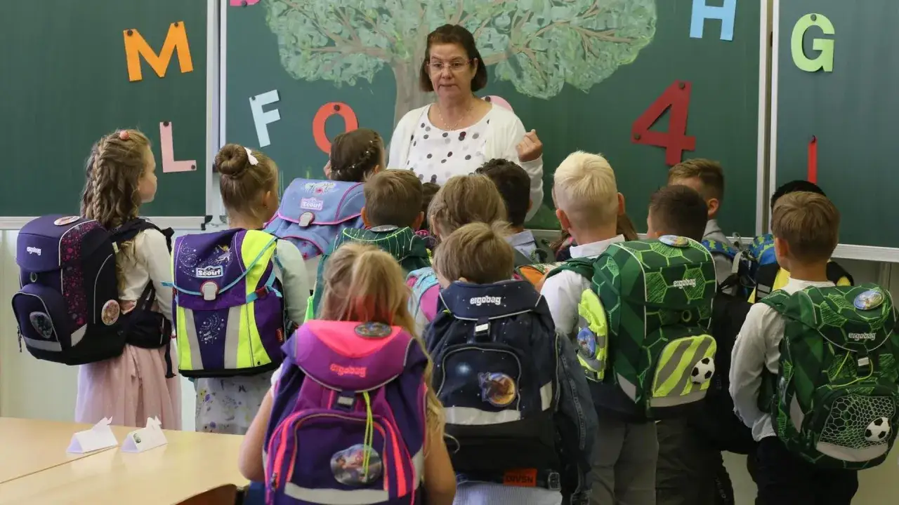 Lehrerin erkl&auml;rt Kindern mit Schulranzen im Unterricht. Die Ganztagsbetreuung Grundschule beginnt mit spannenden Lektionen.