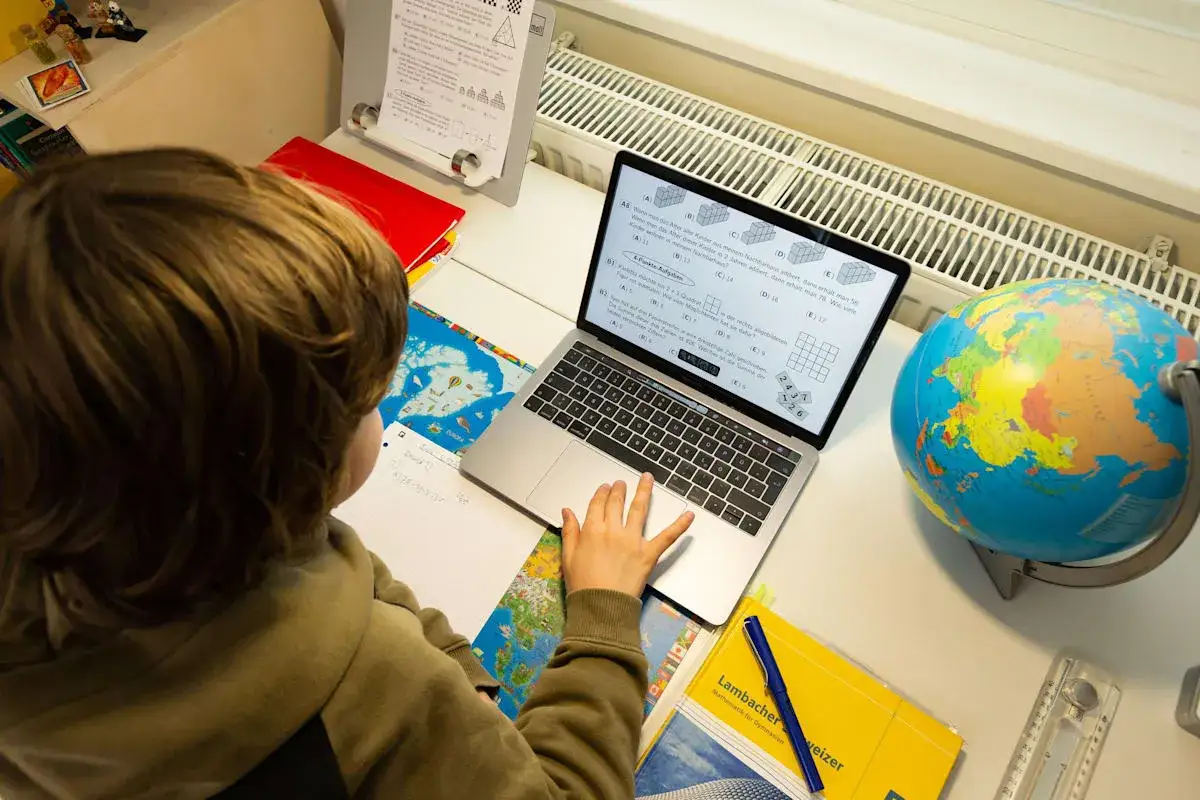 Kind lernt zu Hause am Laptop mit Globus und Schulmaterialien.