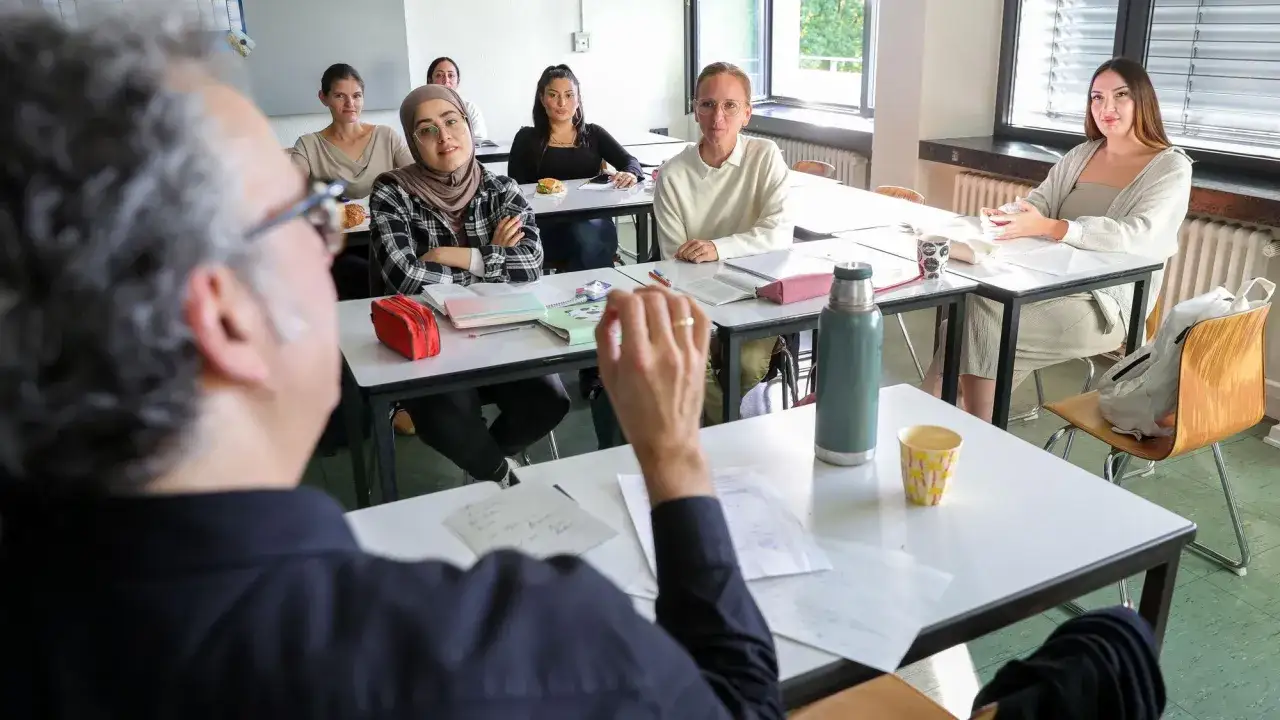 Lehrer erkl&auml;rt Sch&uuml;lern, wie man sein Abi nachholen kann. Sie sitzen im Klassenzimmer, lernen und h&ouml;ren aufmerksam zu.
