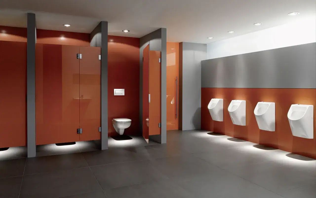 Moderne schul toilette mit orangen Kabinen und mehreren Urinalen.