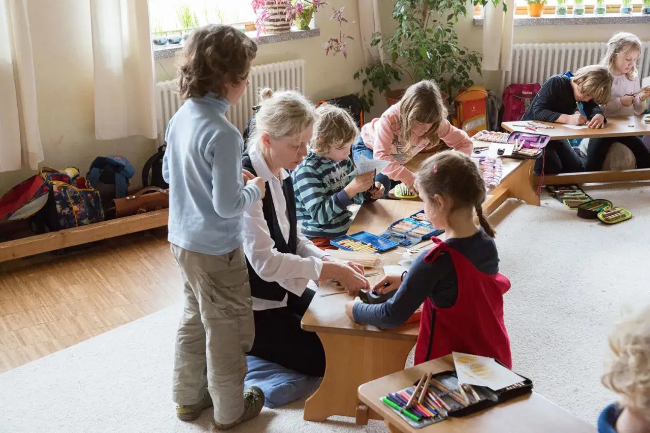 Kinder und Lehrerin basteln und malen. Kreatives lernen in bewegung mit Stiften und Papier.
